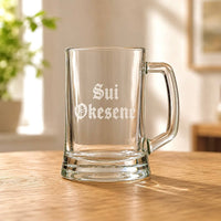 Clear beer mug with engraved Sui Okesene name in Old English font on wooden table