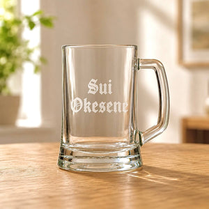 Clear beer mug with engraved Sui Okesene name in Old English font on wooden table
