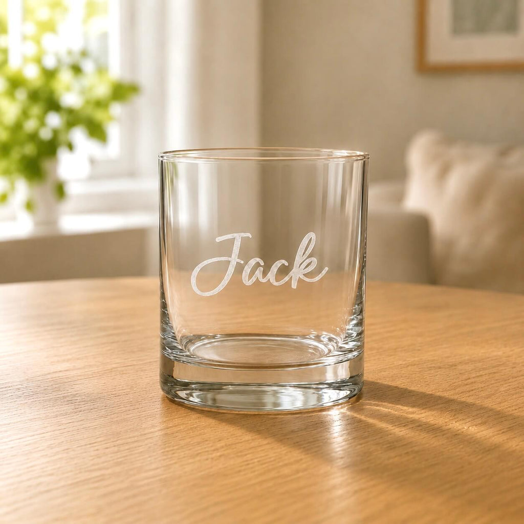 Engraved clear whisky glass with Jack name, rounded rim and wooden table background