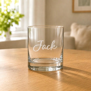 Engraved clear whisky glass with Jack name, rounded rim and wooden table background