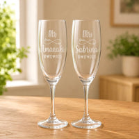 Clear glass Mr and Mrs champagne flutes with engraved names and wedding date on a wooden table